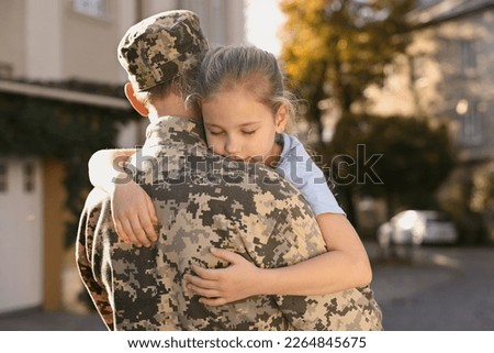 Daughter hugging her father in Ukrainian military uniform outdoors. Family reunion