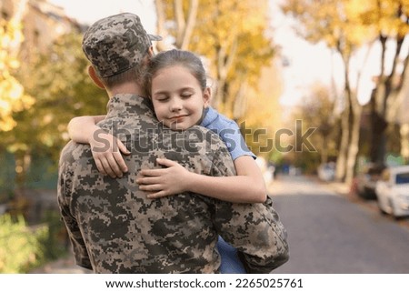 Daughter hugging her father in Ukrainian military uniform on city street. Family reunion