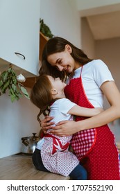 Daughter Hugs Mom In The Kitchen, They Wear Aprons For Cooking