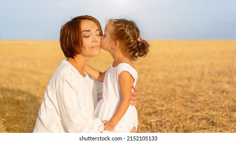 Daughter Kisses Her Mom Cheek Standing Wheat Field. Little Girl Kiss Mother Happy Mother's Day. Happy Family Relationship Outdoor. Dressed White. Caucasian Female Woman 35 Years And Girl 5 Years Old