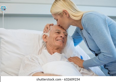 Daughter kissing senior father on forehead in hospital bed. Old dad patient being kissed by daughter while recovering from disease in clinic. Lovely woman visiting old father at medical clinic. - Powered by Shutterstock