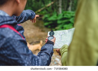 Daughter And Mother Hiking In Forest Using Compass And Map To Navigate