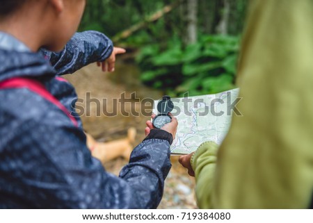 Daughter and mother hiking in forest using compass and map to navigate