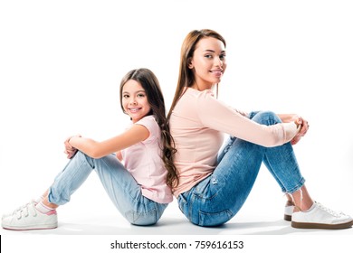 Daughter And Mother Sitting Back To Back And Looking At Camera On White