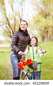 Daughter And Mother Walk Along The Shore Of The Lake In Spring Park With A Bike And Talk. Family Values, Education, Vertical Photo