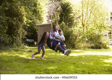 Daughter Pushing Father And Son On Tire Swing In Garden