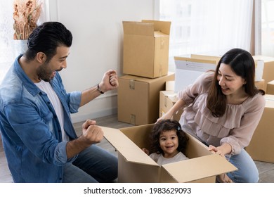 Daughter Sits In A Carton Paper Box Playing With Dad And Mom. The Family Just Moved To A New Home. Parents And Children Have Fun Organizing Things Together.