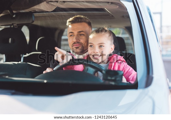 Daughter sitting in car with dad and pointing at car\
window 