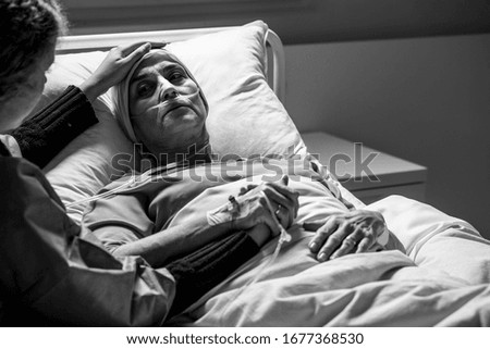 Daughter supporting sad, dying woman with tumor in a hospital, black and white photo
