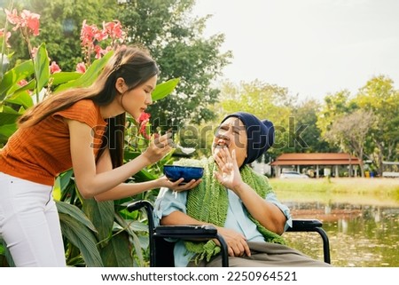 Daughter taking care health elderly mother who is sick with cancer sitting in wheelchair to eat soup to restore body and health but mother is bored of food doesn't want to eat bland food and can't eat Foto stock © 