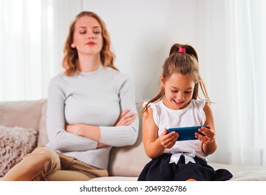 Daughter using a smartphone, while frustrated mother is watching her. - Shutterstock ID 2049326786