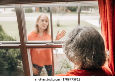 Daughter Visiting Her Elderly Shut-in Mother In Her 80's During Quarantine From Covid-19 Coronavirus Through A Window