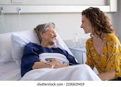 Daughter visiting sick old mother in hospital. Happy senior patient smiling while in conversation with her lovely daughter. Granddaughter visiting and cheering her hospitalised grandmother in bed. - Powered by Shutterstock