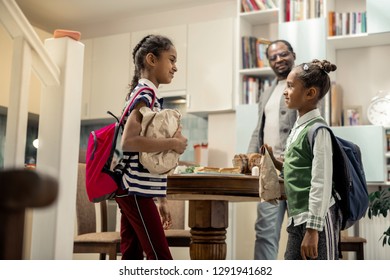 Daughters With Backpacks. Two Cute Stylish Daughters With Backpacks Leaving Home To School With Lunchboxes