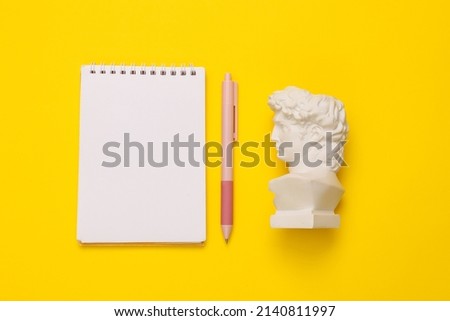 David bust with notebook on yellow background. Minimal still life photo