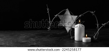David star, barbed wire and burning candle on dark background with space for text. International Holocaust Remembrance Day