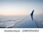 Dawn above the clouds - window seat view. Perspective view of airplane wing. Sunrise at the height of 10 000 meters in the background.