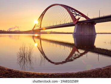 Dawn Of The Bugrinsky Bridge. Arched Modern Automobile Bridge Over The Ob River In The Golden Morning Light, The Rising Sun, Reflections In The Water. Novosibirsk, Siberia, Russia