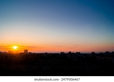 Dawn in a clear summer sky over the city. The rising sun breaks through light clouds on the horizon. Silhouettes of buildings in backlight - Powered by Shutterstock