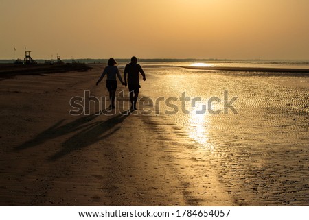 at dawn a  couple of lovers strolls on the beach holding hands