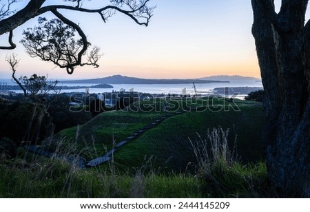 Dawn at Mt Eden summit with volcanic crater in the foreground. Rangitoto Island framed by Pohutukawa trees. Auckland.