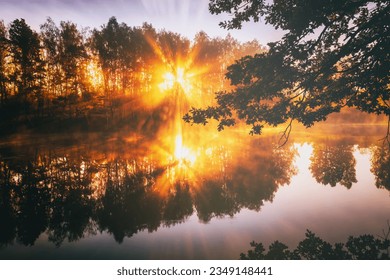 Dawn on a lake or river with a dramatic cloudy sky reflected in the water, birch trees on the shore and the sunbeams breaking through them and fog in autumn. Aesthetics of vintage film.