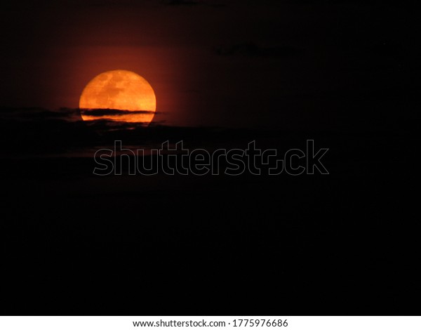 Dawn of an orange moon among the clouds. Orange\
moon between the clouds.