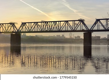 Dawn over the bridge over the Ob. Early morning on the great Siberian river, Golden dawn with clouds, a city on the Bank in the distance, a railway bridge in the capital of Siberia, reflections