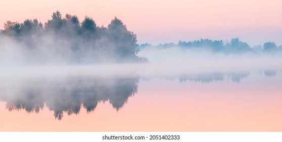 Dawn over the foggy lake. Beautiful dreamy view. Pink sky just before the sunrise and fog over water and trees with reflections on the river bank. - Powered by Shutterstock
