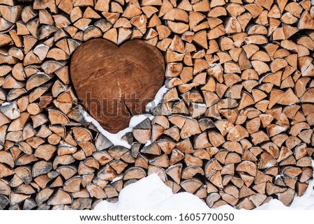 Valentine’s Day background. Wood for the fireplace arranged in an artistic way with a wooden heart in the middle. Winter scenery with snow around. Natural, wooden 
