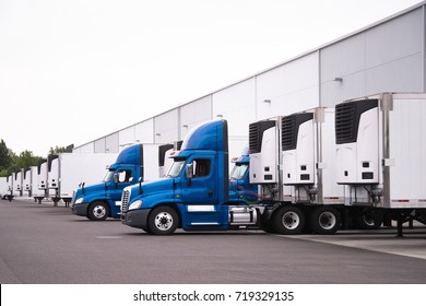 A day cab big rigs semi trucks with a reefer trailers stand near the gate of the warehouse next to other reefer trailers that are loaded and unloaded to deliver perishable and frozen food to consumers