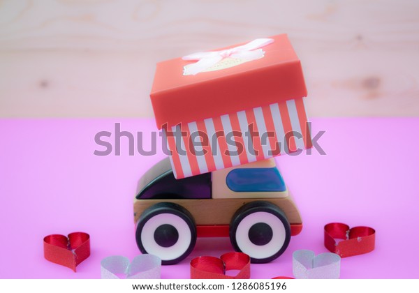 Valentine’s Day concept, A toy car\
delivering gift box for Valentine\'s day on pink\
background.