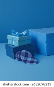 Father’s Day gift setup with two stacked gift boxes—one light blue with a satin ribbon, the other navy—accompanied by a rolled-up blue and burgundy checkered necktie. Ideal for Father's Day, birthdays