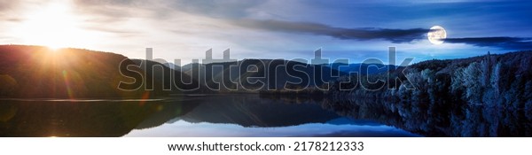 day and night time\
change above beautiful autumn landscape by the lake. trees on the\
shore and forested mountains reflecting in the water surface. sun\
and moon above horizon