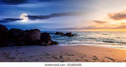 Day And Night Time Change Concept Above Huge Stones On The Sandy Beach At Twilight. Wonderful Velvet Season Vacation. Clouds On The Blue Sky With Sun And Moon Above Horizon. Waves Washing The Shore