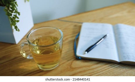 Day Summing In Bullet Journal Planner In Evening Light Room. Close-up, Herbal Tea In Glass Cup. Open Paper Diary On Wooden Table Lies With Notes, Pen Lies On Pages. Year Sum Results