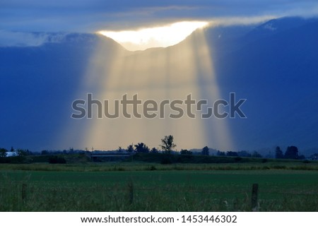 Daybreak and a gap in the thick clouds allows a bright spotlight of sunlight to stream onto the agricultural, rural countryside. 