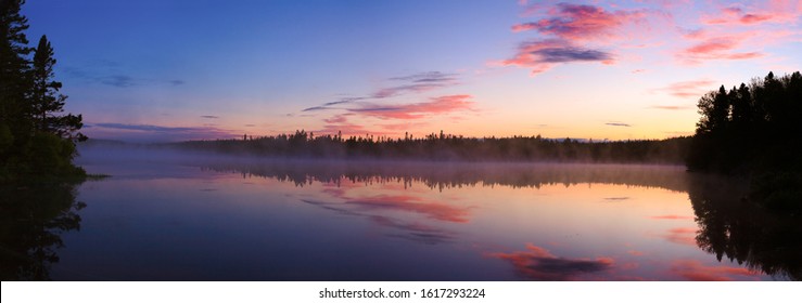 Daybreak reflections on a calm lake. Wide format image.