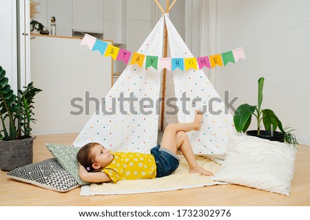 Daydreaming happy little girl lying on a blanket in front of a hut, made with sticks and bedsheets. Her mind wanders far away in a magical land.