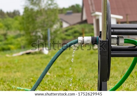 Daylight. in focus the fitting drips water from it. Near a hose reel.