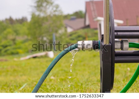 Daylight. in focus the fitting drips water from it. Near a hose reel.