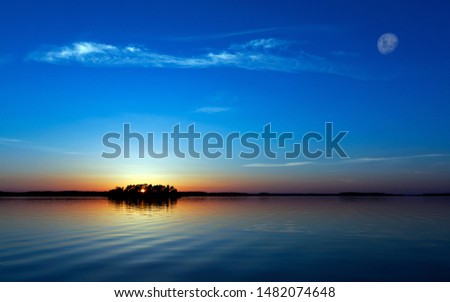 Daylight moon appears in the evening sunset time. A moody tropical beach sea water around the island. A beautiful Cloudy weather with orange yellow coloured in the blue sky. Bluesky in theSunset time.