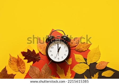 Daylight saving day. Fall Back. Black Alarm clock and autumn leaves on yellow background. Daylight saving time end