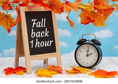 Daylight Saving Time fall back sign with alarm clock and standing blackboard on weathered wood with fall leaves - Shutterstock ID 2057655848