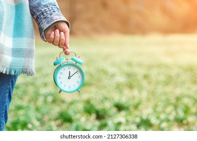 Daylight Saving Time Reminder. Spring Time Change Background. The First White Spring Snowdrops. Early Spring Weather. Woman Holding Alarm Clock Over Spring Flowers Background.