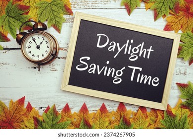 Daylight Saving Time typography text on wooden blackboard with alarm clock and maple leaves