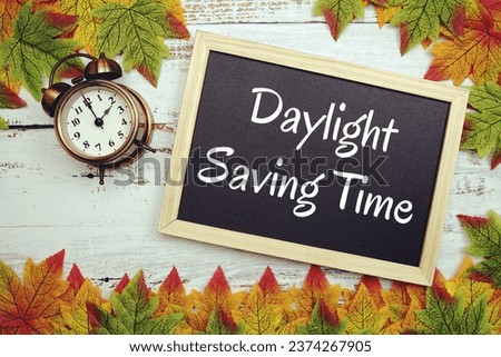 Daylight Saving Time typography text on wooden blackboard with alarm clock and maple leaves