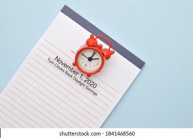 Daylight Savings Clock And Notepad On Light Blue Background