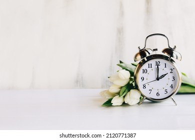 Daylight savings time concept. Set your clocks and to 2 am and spring ahead with this image of an alarm clock with white tulip flowers. Selective focus with blurred foreground and background.