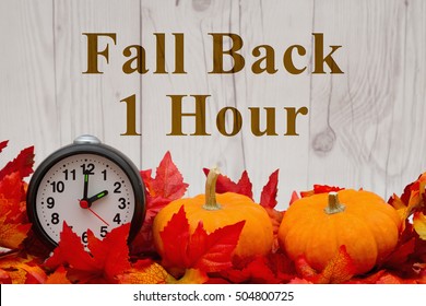 Daylight Savings Time Message, Some Fall Leaves And Retro Alarm Clock And Pumpkin On Weathered Wood With Text Fall Back 1 Hour